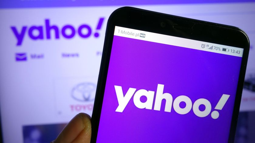 A hand holding a phone showing the Yahoo logo on a purple background