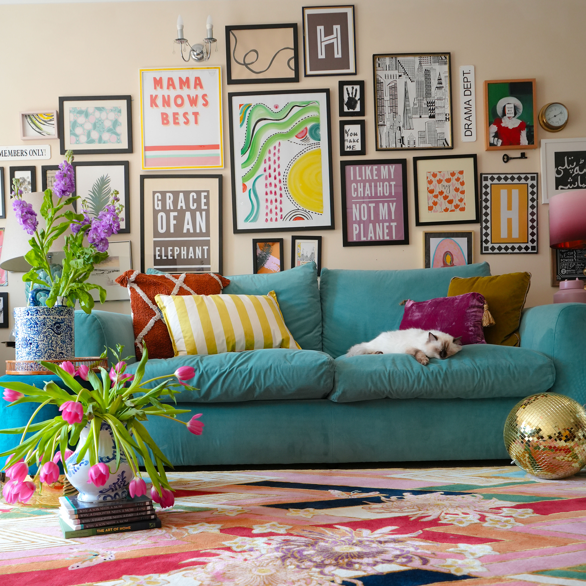 gallery wall full of art in an assortment of frames, arranged on a beige wall above a bright blue sofa