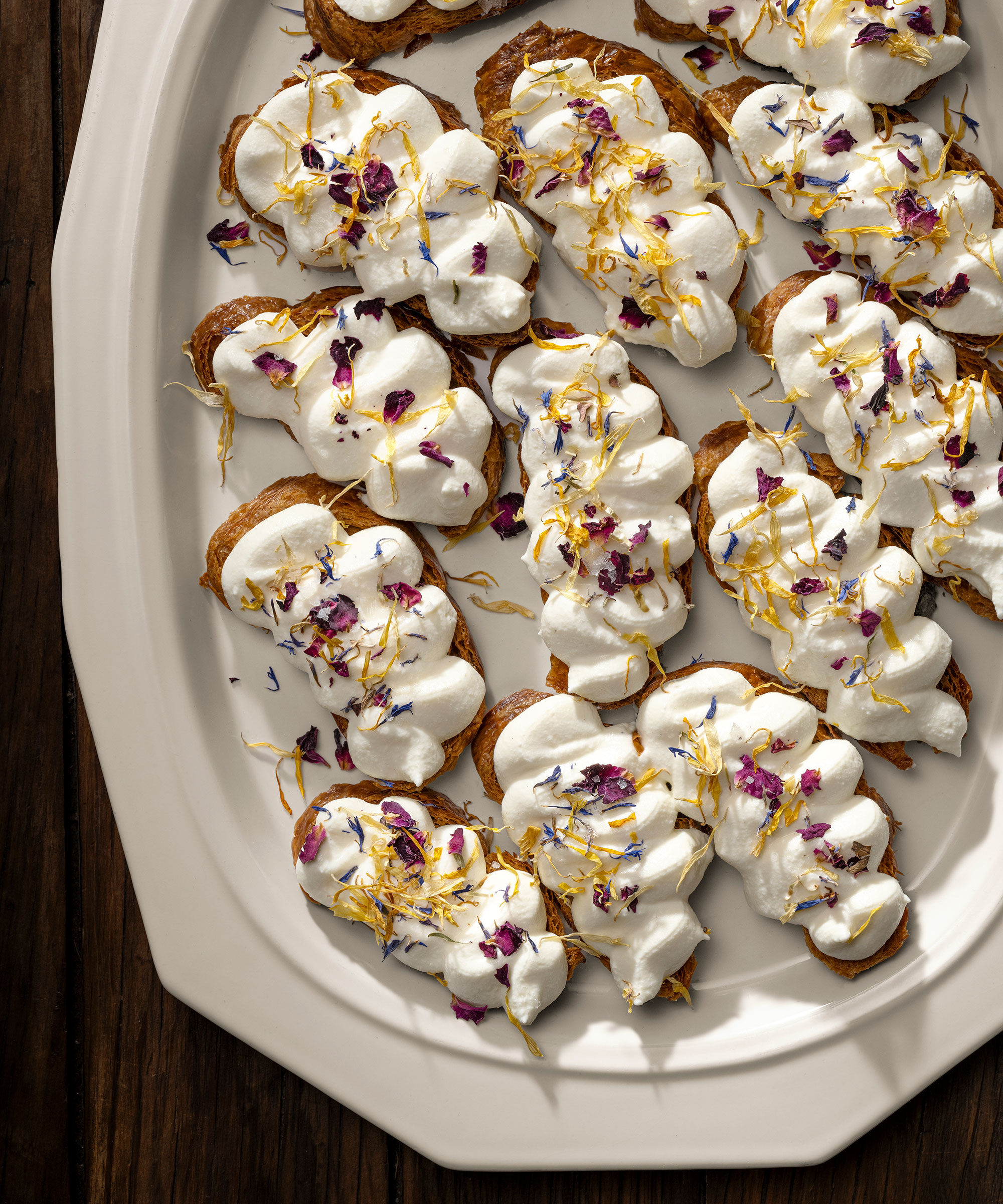 A high-angle, close-up shot of several whipped ricotta crostinis arranged on a large, white ceramic platter.