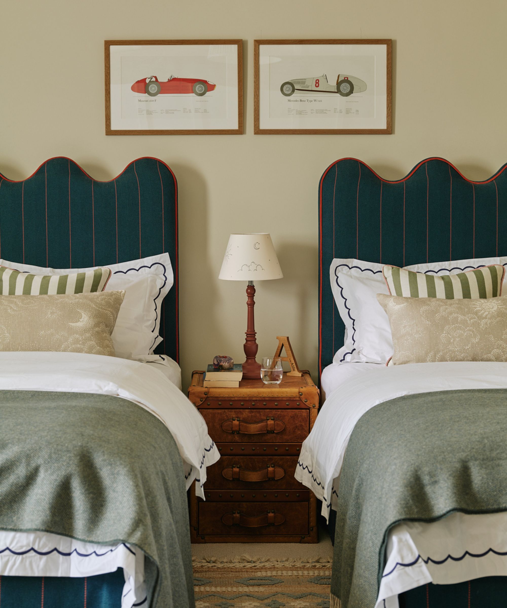 A bedroom with twin beds with teal headboards, cream walls and artwork on the wall.