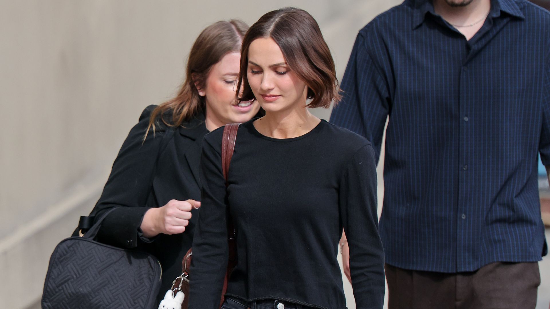 Maude Aptow wears black baggy jeans with a black longsleeve top and black heeled ballet pumps.