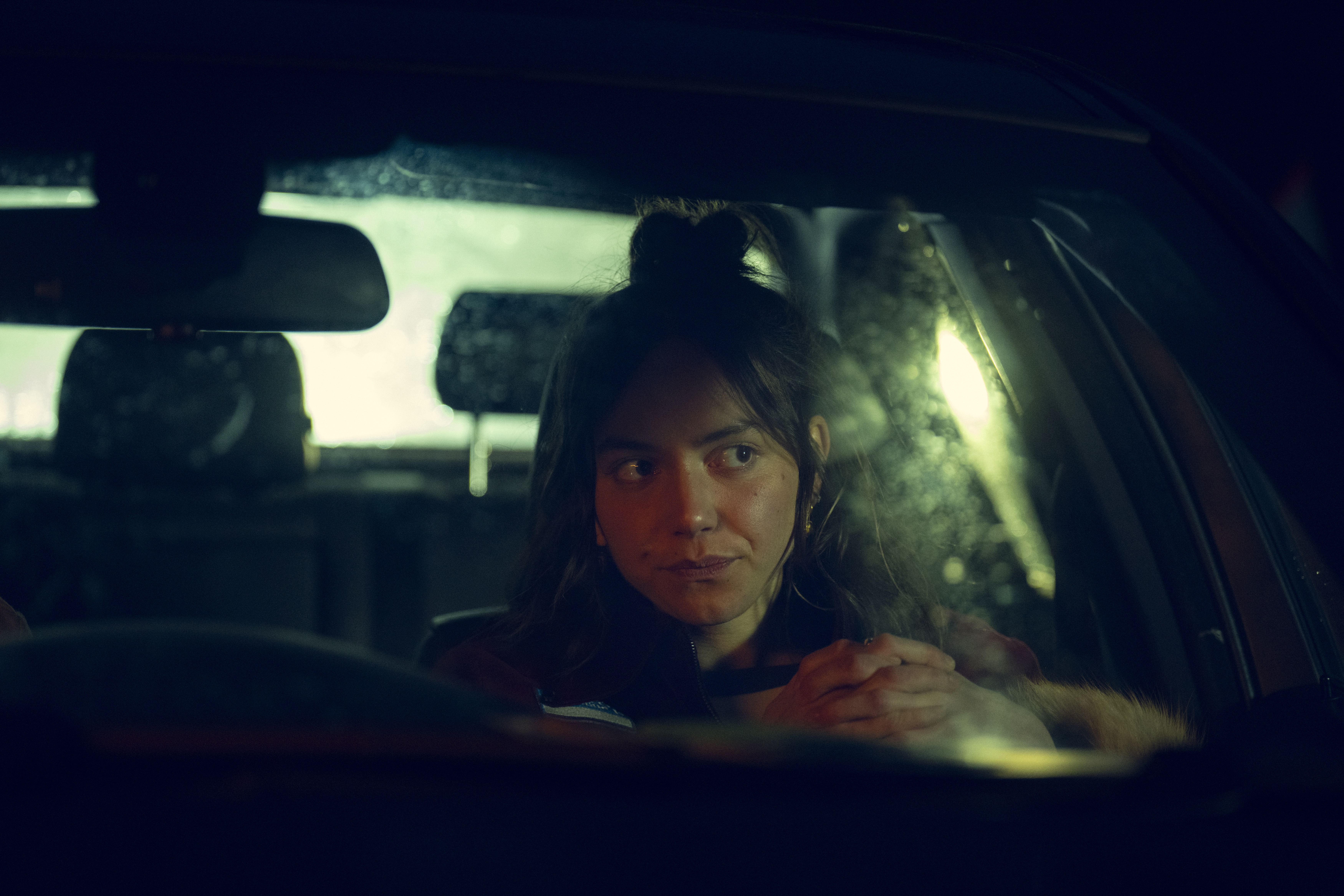 Maeve Courtier-Lilley as dee dee looking suspicious sitting in the front seat of a car at night time in Run Away