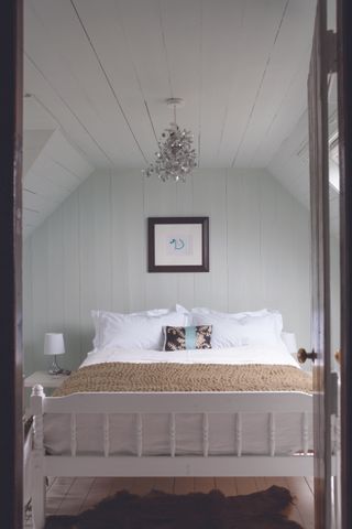 How to make a small bedroom look bigger in a pale green bedroom in an attic with wood panelling and white double bed