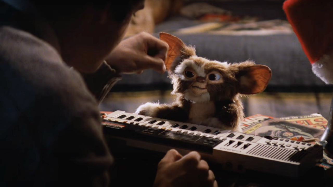 Gizmo sits smiling at a keyboard with Zach Galligan in Gremlins.