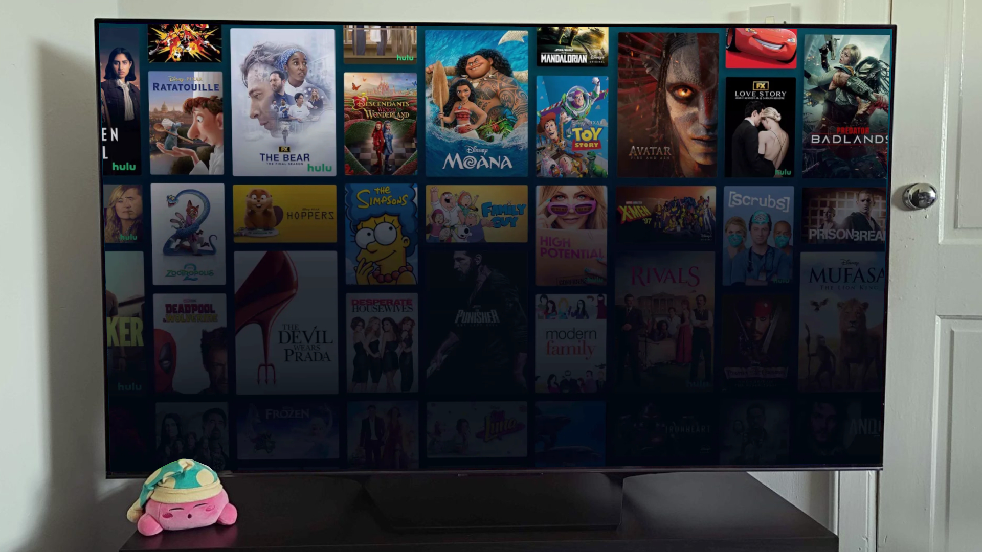 A screen displaying Disney Plus and Hulu content, with a sleeping Kirby plush visible in the bottom left-hand corner