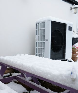 heat pump outside home in winter with picnic bench table covered in snow