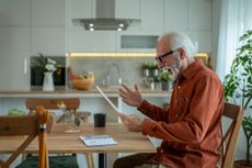Stressed mature man looking surprised while reading a letter with bad news, sitting at dining table in his modern apartment, holding his head in disbelief