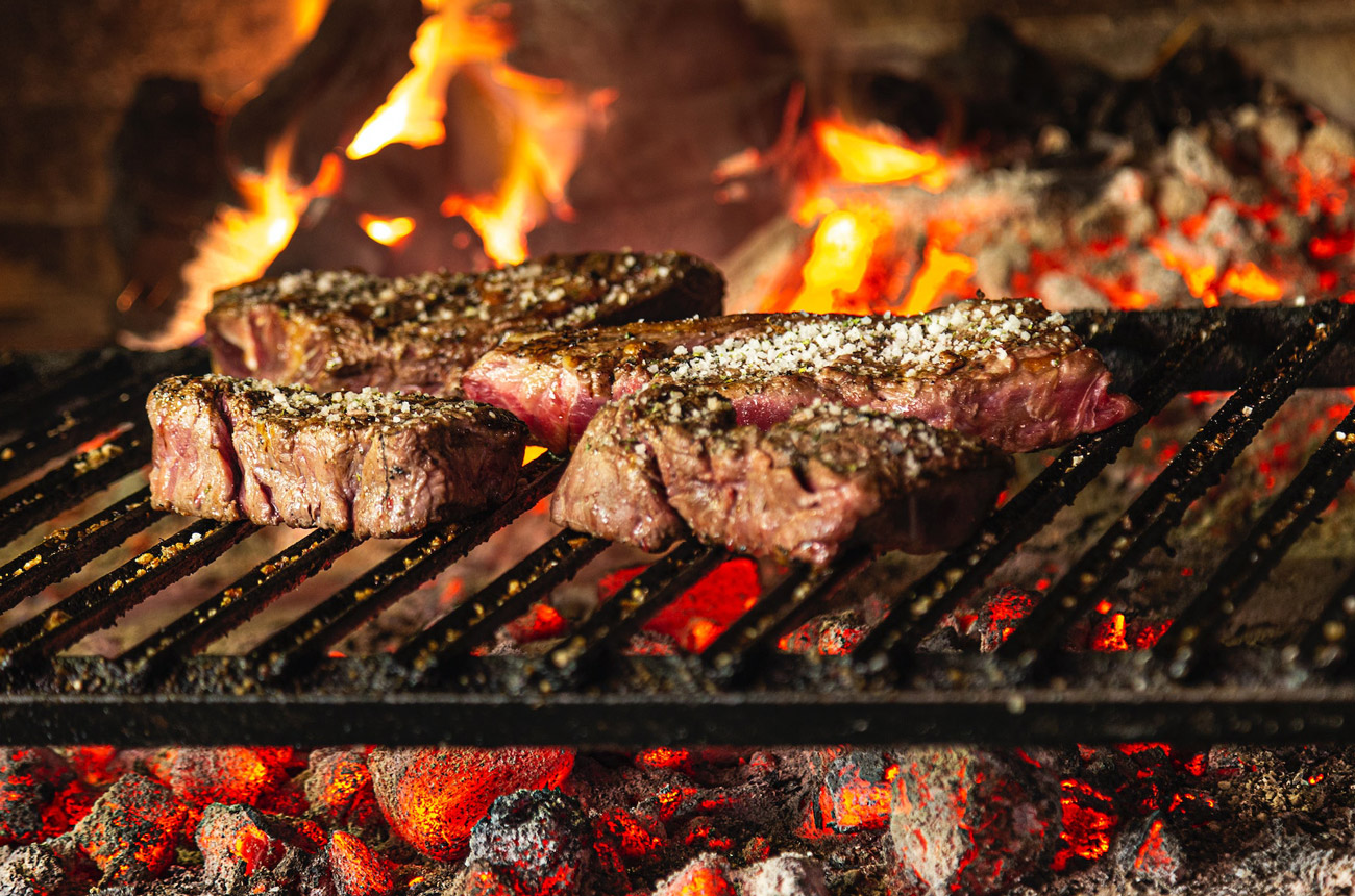 Steak cooking on a grill over flaming charcoal