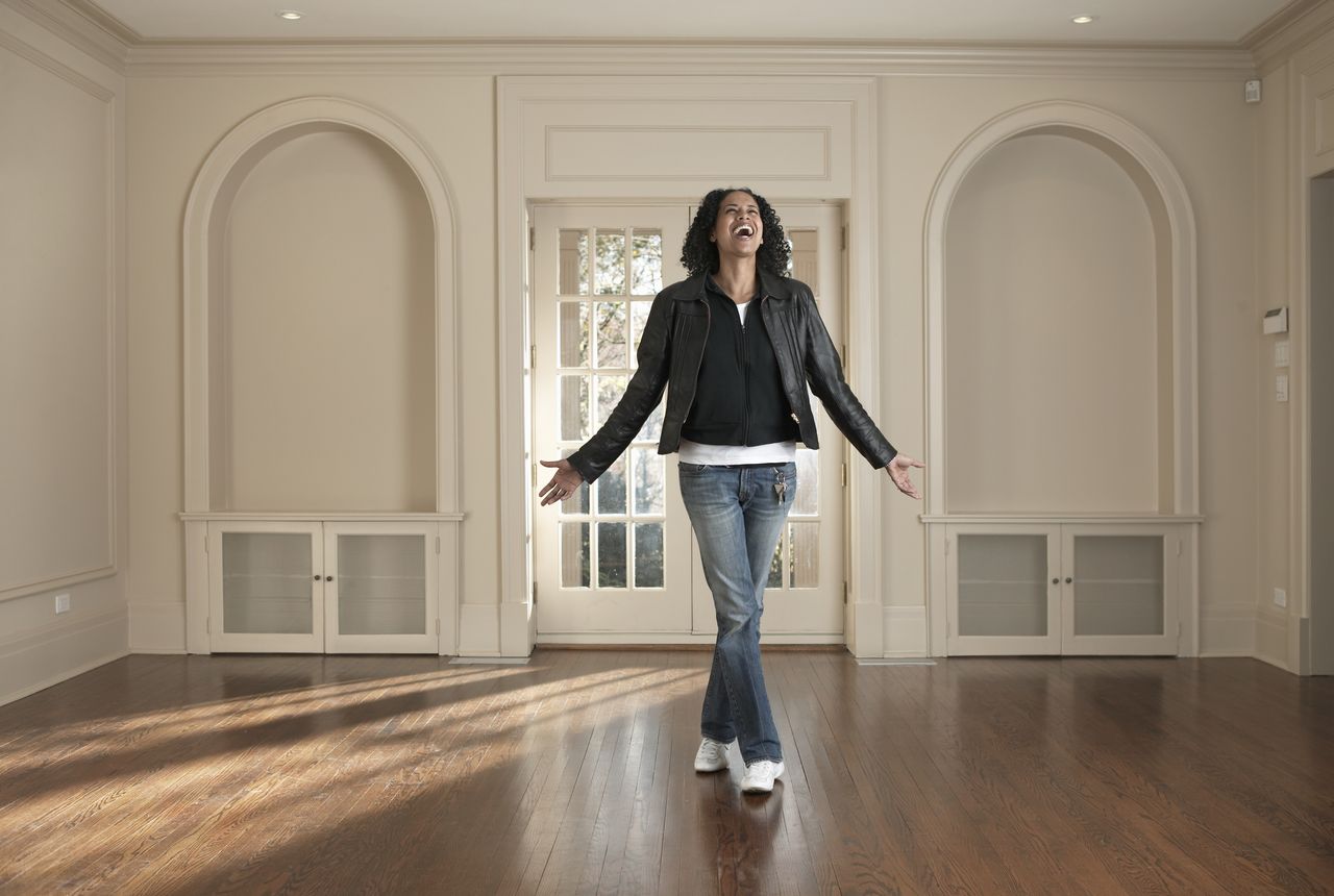 Woman standing in new home, smiling with arms outstretched.