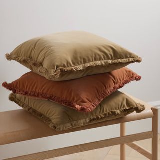 stack of three beige and rust-colored cushions with fringed edge