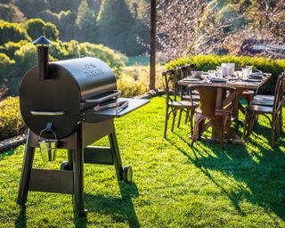 A bbq on a lawn with an outdoor dining table set for dinner