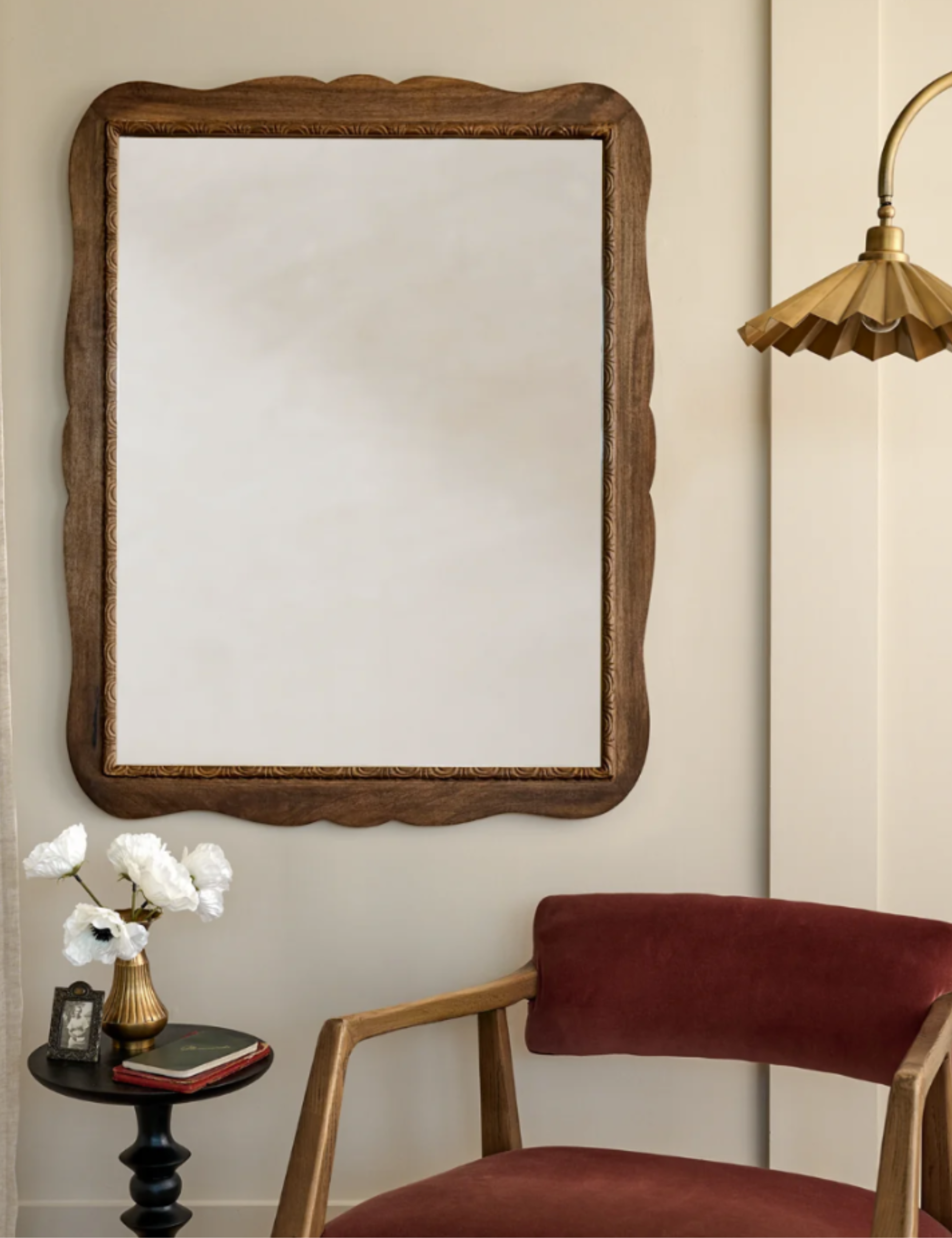 Seating area vignette featuring a red velvet-upholstered mid-century-style accent chair, brass floor lamp, and antiqued scalloped wooden wall mirror
