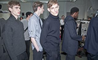 A line of male models wearing smart casual clothing, one turning and winking at the camera