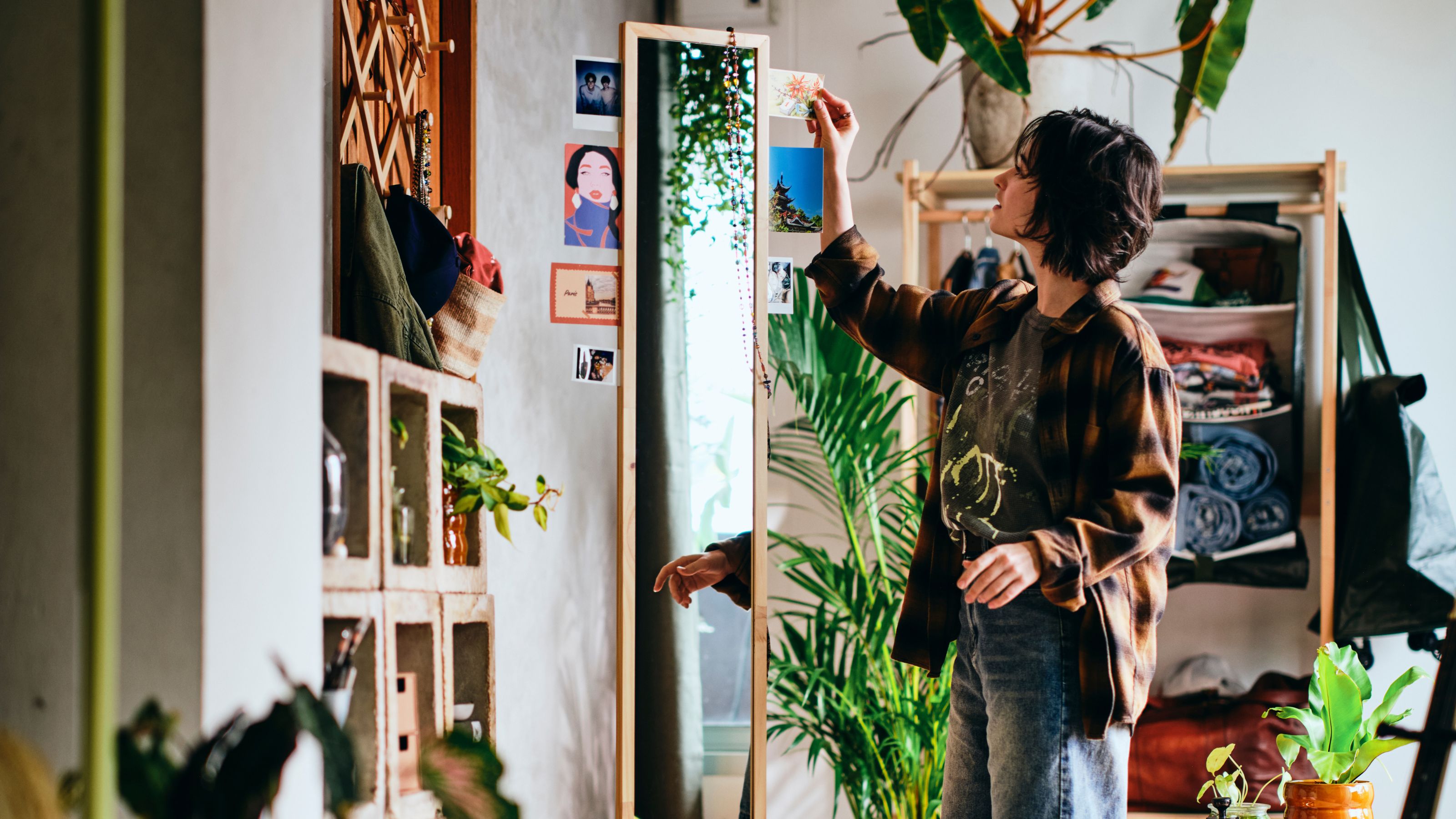 IKEA KOMPISHANG Standing Mirror in a room filled with storage and plants with a woman adding pictures into the inserts along the sides of the mirror