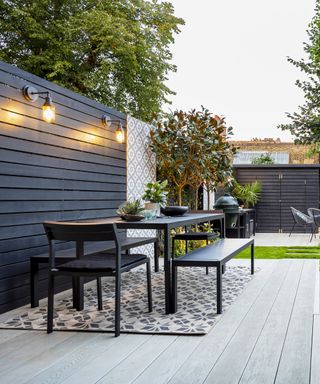 A contemporary patio with wall lights mounted on a dark fence