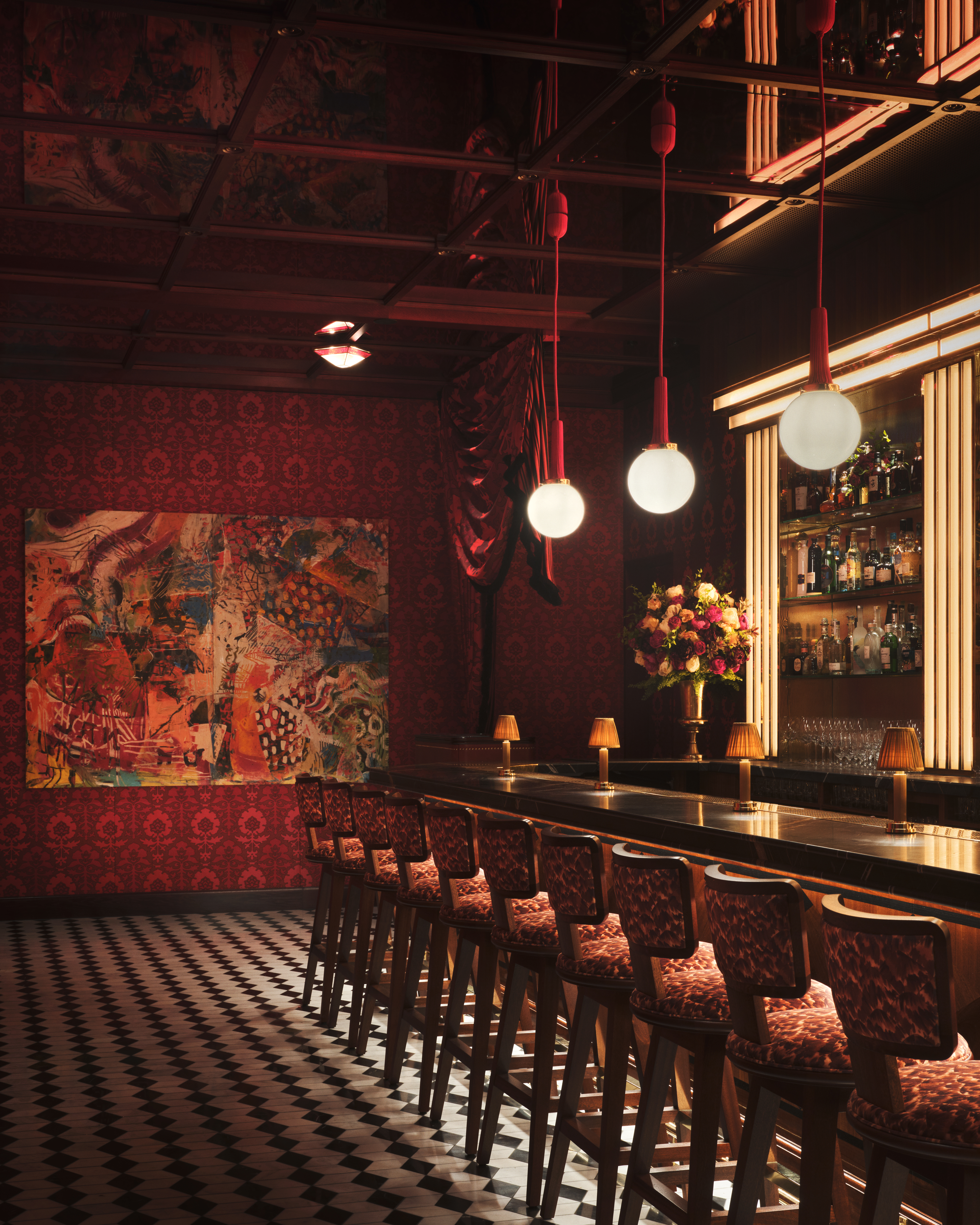 A dazzling decorated restaurant with checkered, red and white marble floors, red velvet drapery, banquettes, and leather chairs, ciambella-shaped lighting with a golden glow, and softly burning table lamps.