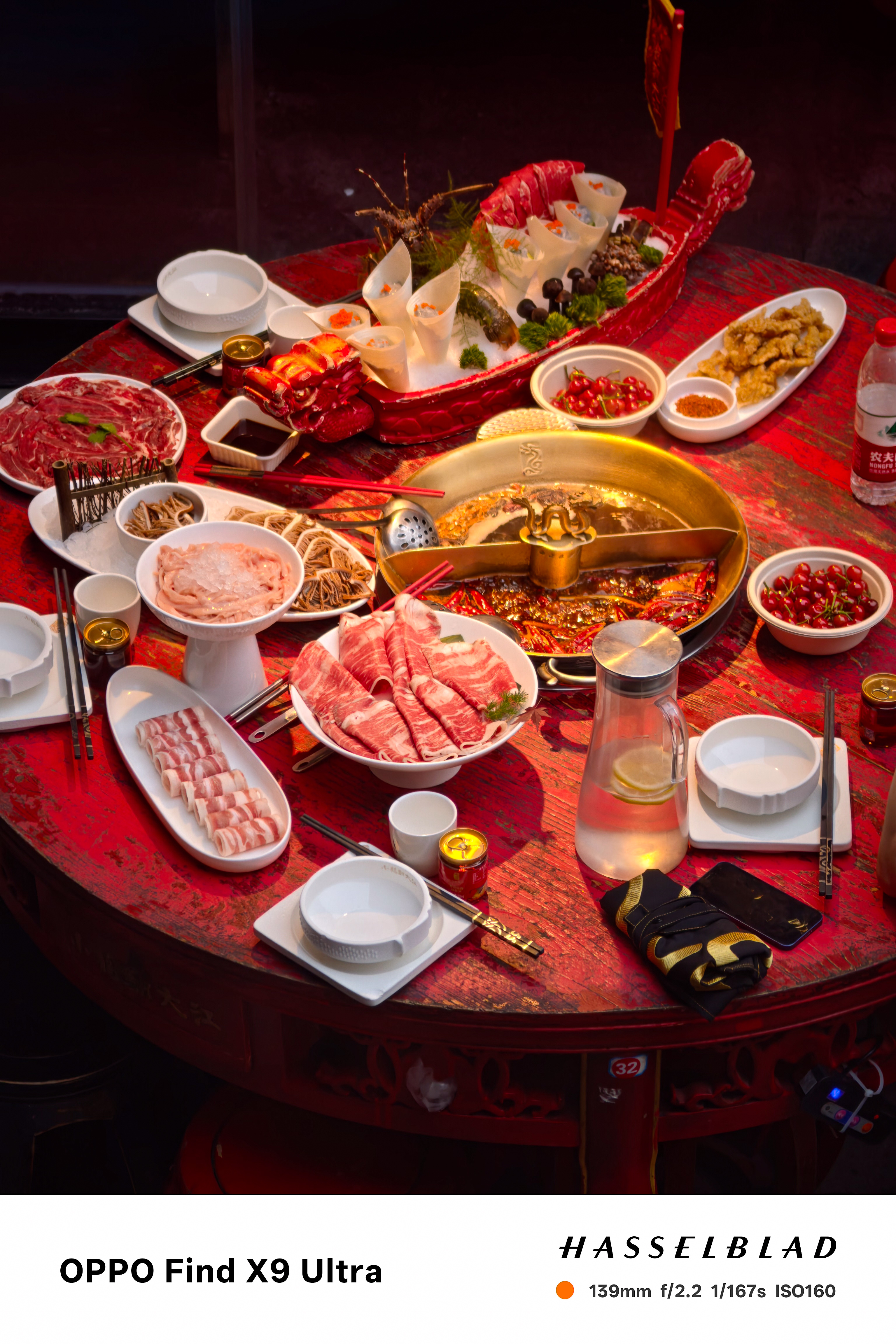 Red table crowded with hot pot dishes, meat platters, and a divided broth pot