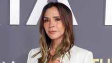 Image of Victoria Beckham smiling with curly brunette hair and wearing a white blazer