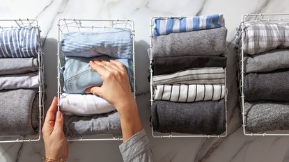 Neatly folded clothes and pyjamas in the metal mesh organizer basket on white marble table. 