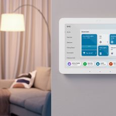 Amazon Alexa Echo hub attacxhed to a wall baide a living room with a floor lamp and sofa in the room