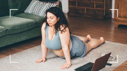Woman using one of the best yoga apps, lying down in yoga position on mat in living room with laptop next to her, eyes closed