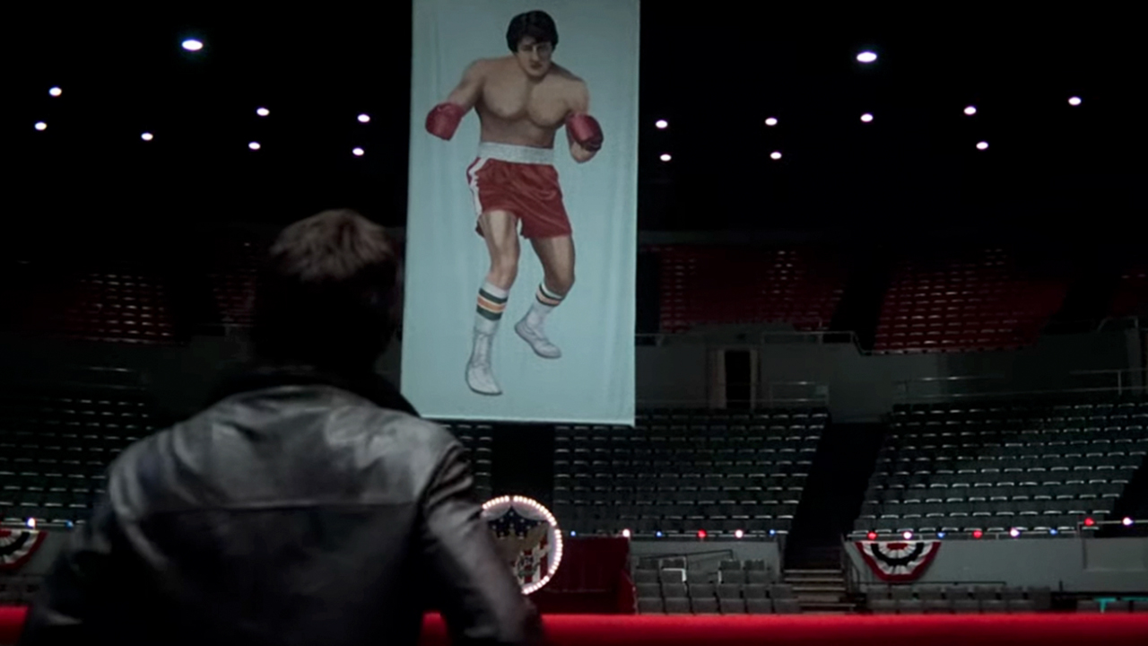 Rocky, from behind, looking at a banner of himself wearing red shorts