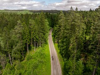 Drone shot of gravel cyclists riding through a coniferous forest in Sweden