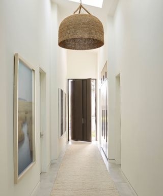 Minimalist narrow white hallway, pendant, rug, artwork on walls