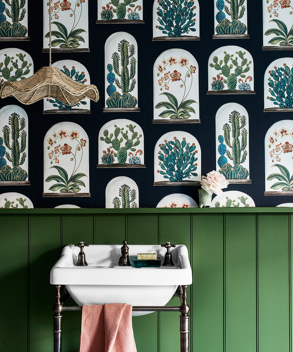 A green paneled wall with botanical imagery above it behind a white traditional sink