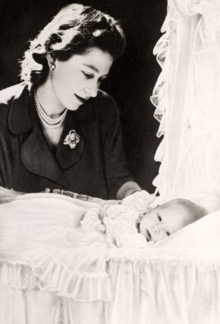 The Queen and Prince Charles as a baby laid in a crib
