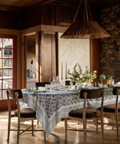 Spring tablescape with rattan pendant light, printed floral tablecloth, wooden chairs, flowers and candles