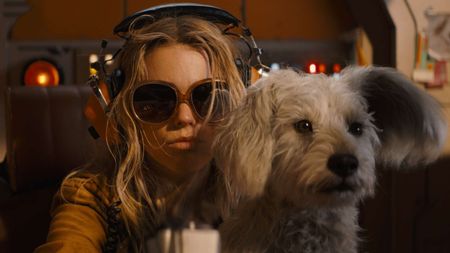 Kara wearing sunglasses and headphones while sitting in a cockpit with Krypto on her lap in Supergirl
