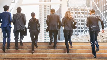 Six businesspeople run side by side up a flight of steps outside a skyscraper.