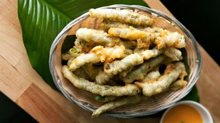 Tempurafriterade grönsaker ligger i en skål på ett stort grönt löv på ett träfärgat bord.