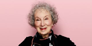 Margaret Atwood seen from the shoulders up, smiling against a pink background