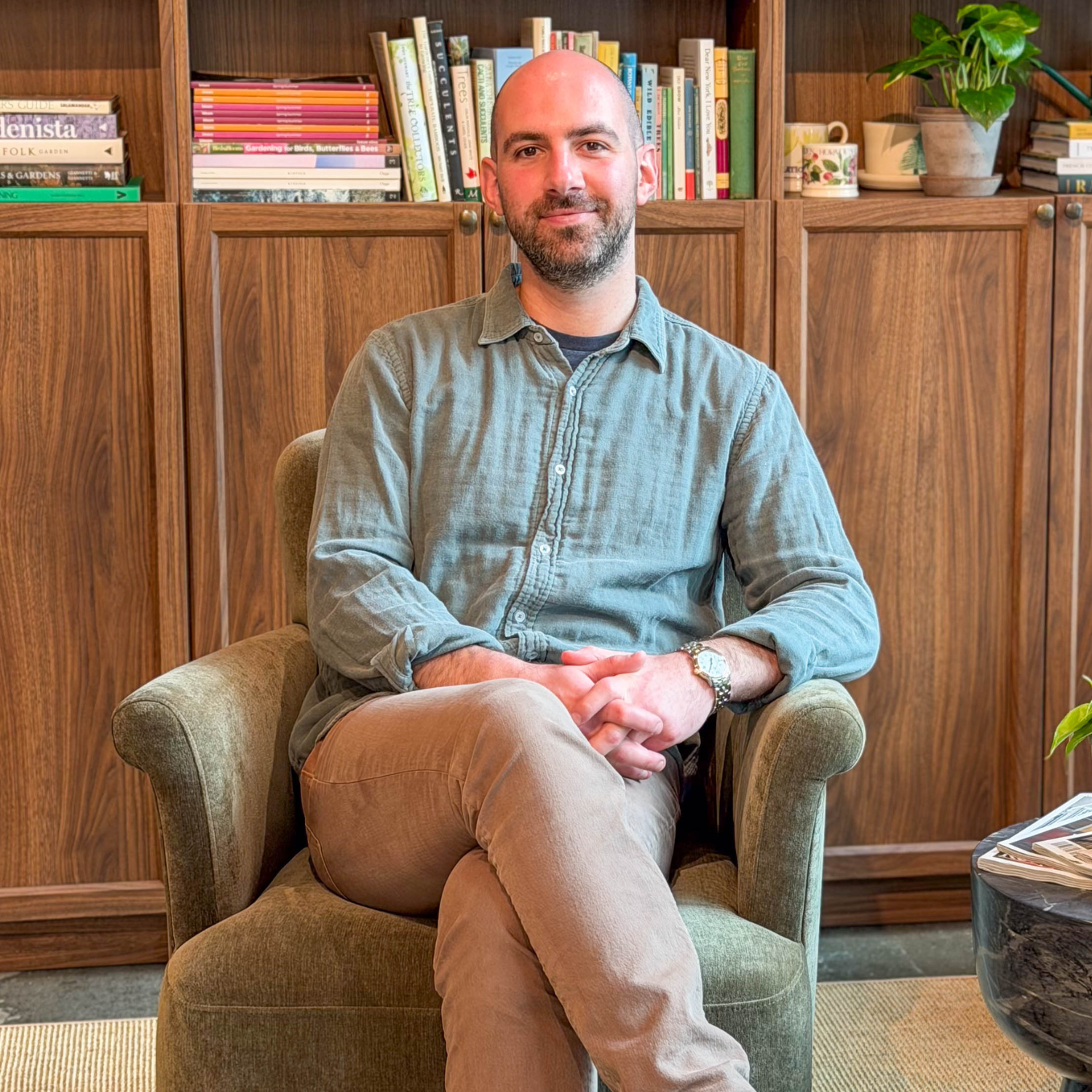 A headshot of a man in a green shirt and tan pants in a green armchair