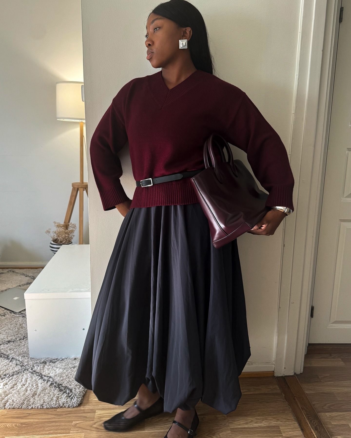 Influencer @nnennaechem wears a v-neck burgundy jumper with a black balloon skirt and mesh ballet flats.
