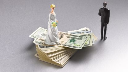 A bride's figurine sits on a stack of $20 bills while the groom's figurine appears to be walking away.
