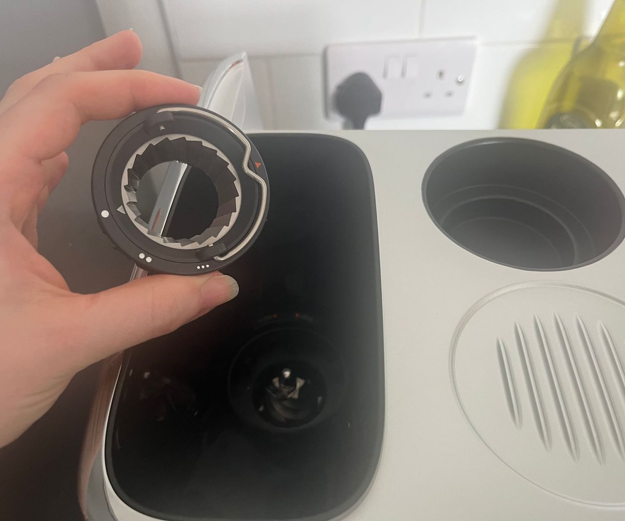 The top part of a conical burr coffee grinder being held above the bean hopper of the Ninja Luxe Caf&eacute; Mini espresso machine.