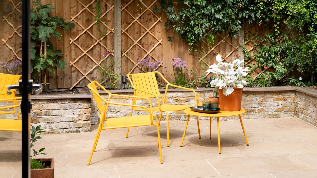 A patio with a bright yellow garden chair set with a matching table