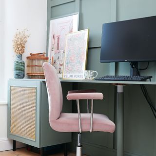 Home office with pink desk chair, floral artwork and green painted wall panelling