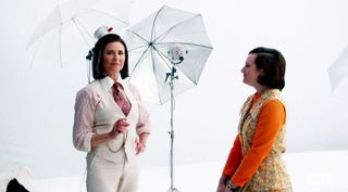 Woman in white 3-piece suit standing with woman in orange