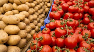 A greengrocers stall with potatoes and tomatoes stacked next to each other.