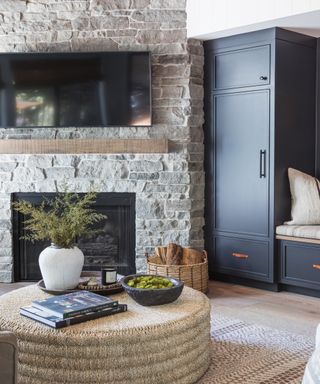 Brick corner fireplace in living room with blue cabinets, woven coffee table and rugs