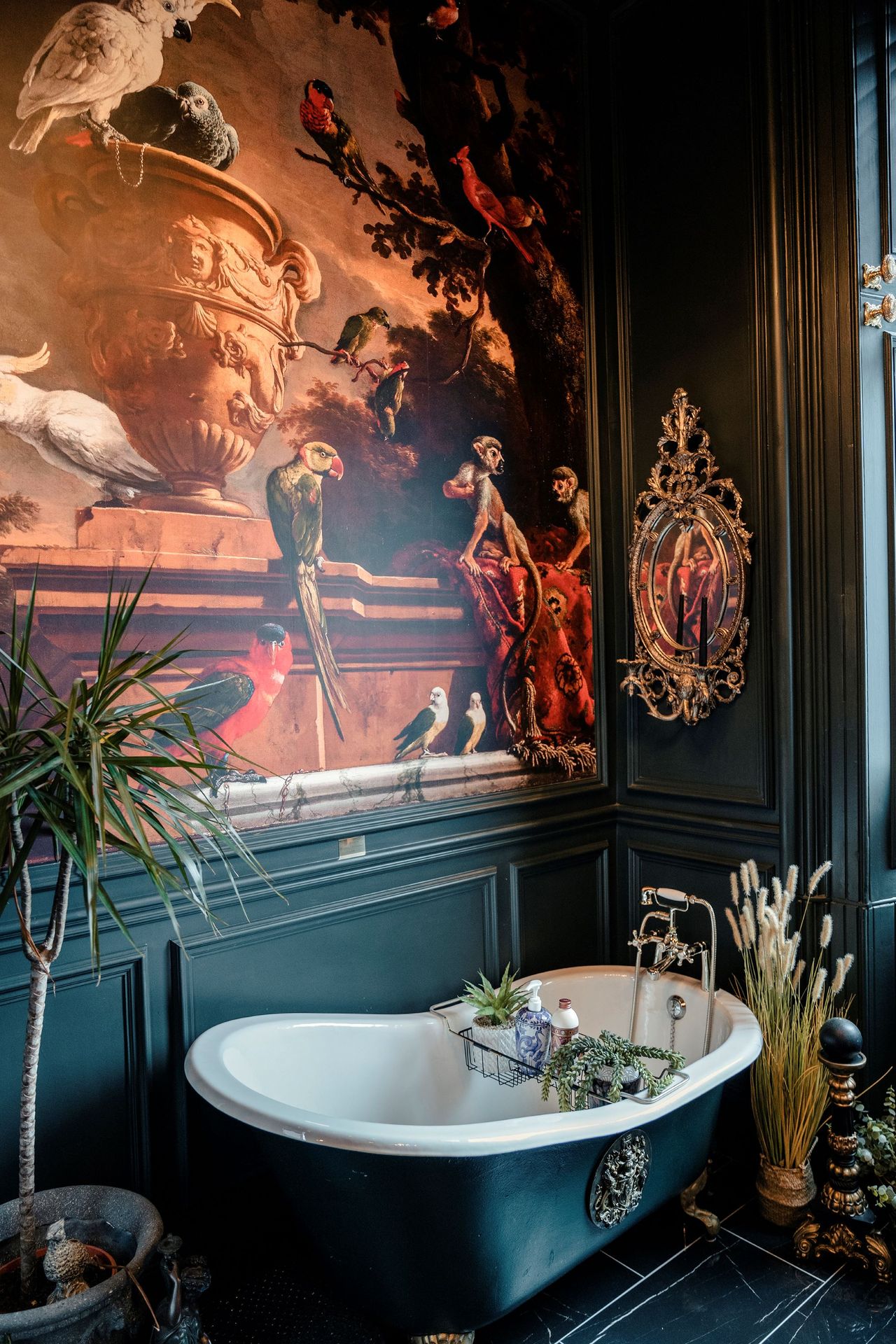 The bathroom has a mural on the wall of many exotic birds and monkeys which covers the entire wall next to the black curved bath