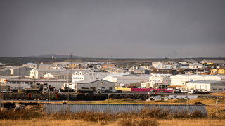 View of Grindavik, a small fishing village in iceland with white buildings in the distance, under grey sky and dried brown grass
