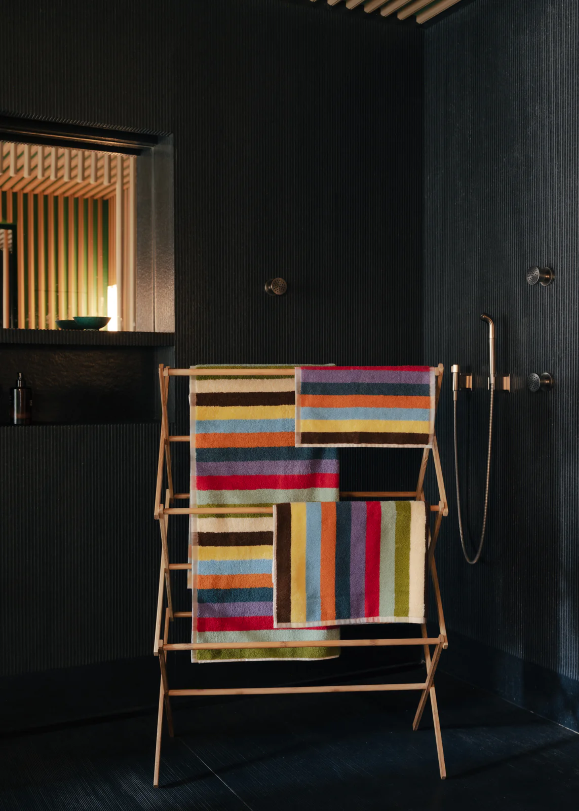 A black shower room with a drying rack loaded with striped towels