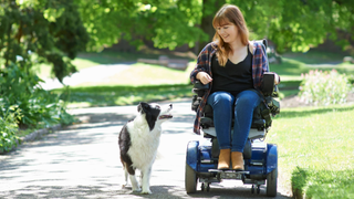 Woman sitting in a wheelchair in a park with a dog looking up at her beside her
