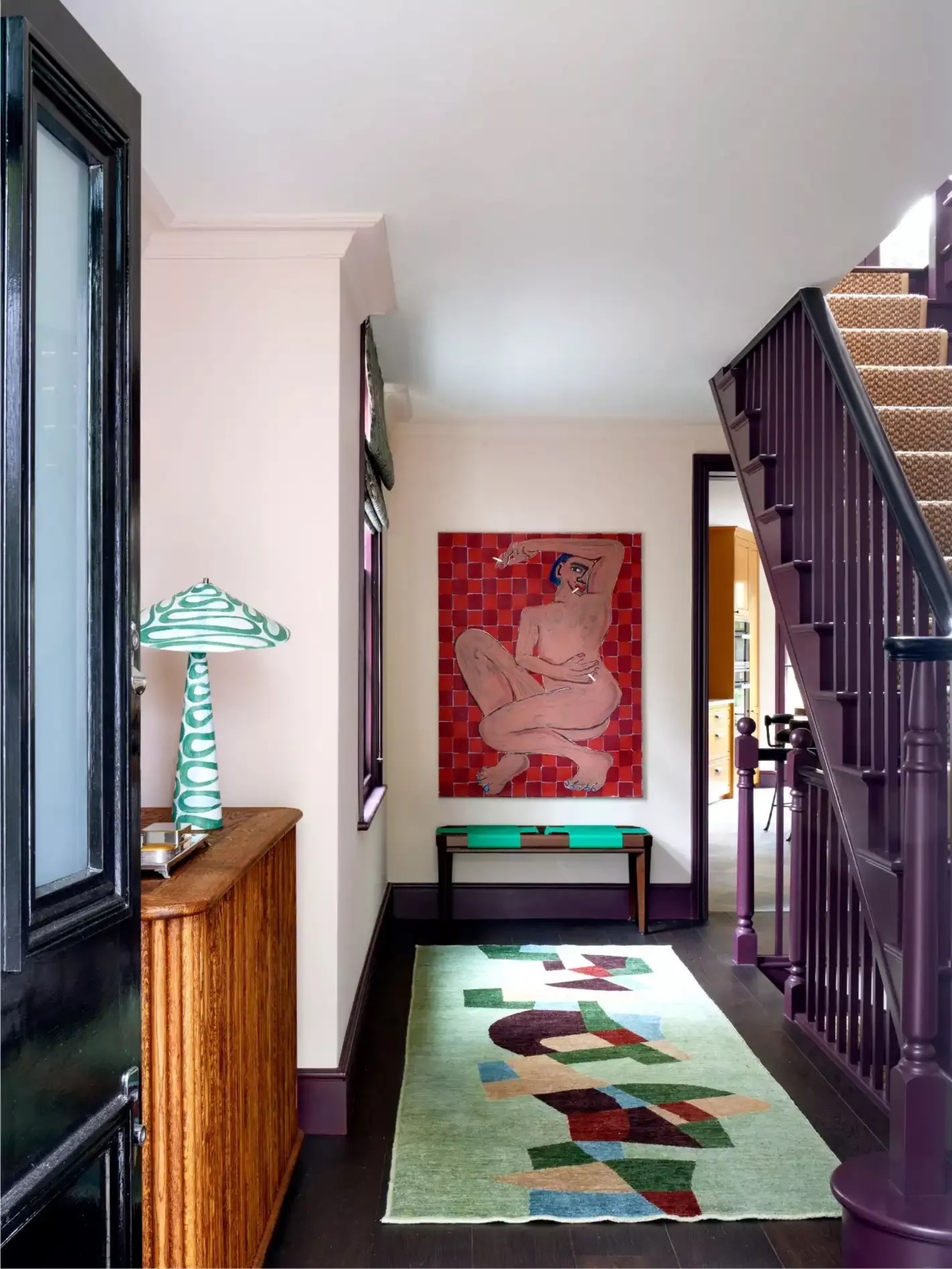 hallway with purple-painted staircase, pink walls, timber console with green striped table lamp, with colorful sage hallway runner, with large artwork on the wall at the end