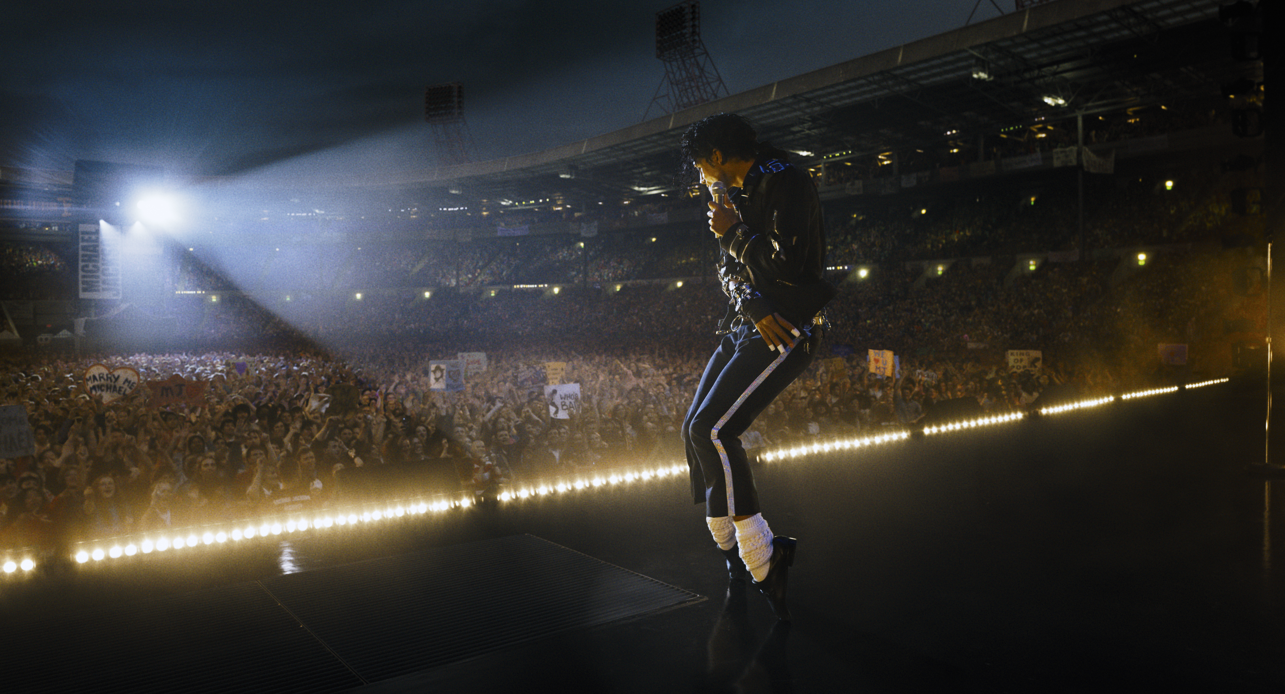 A man (actor Jaafar Jackson as Michael Jackson) stands on his toes while dancing onstage in front of a crowded stadium, in the 2026 biopic 'Michael.'